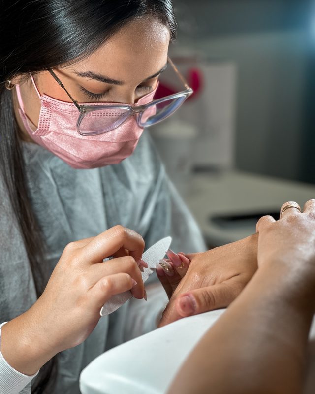 Profissional aplicando cílios, de máscara rosa.